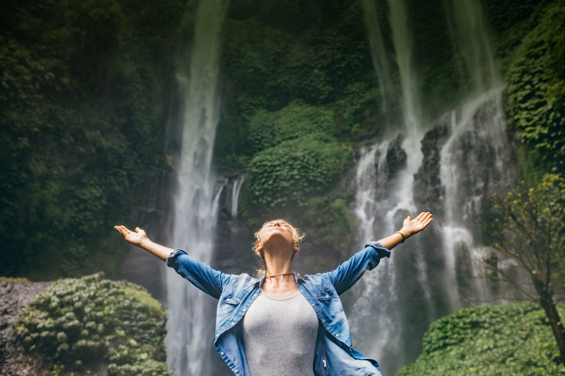 Person standing with arms raised before a waterfall in nature