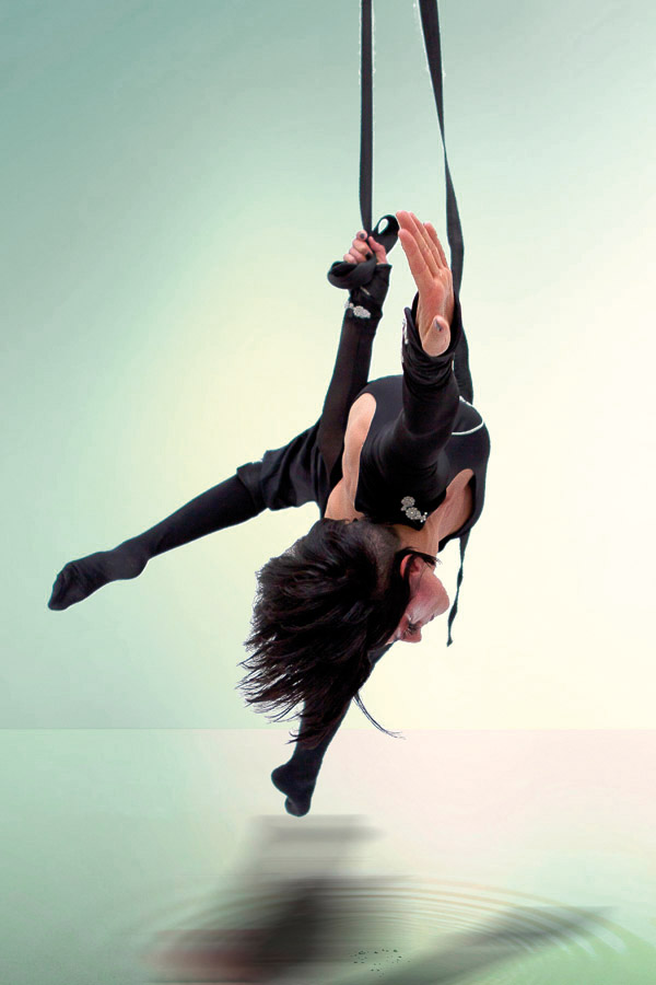 Aerial acrobat mid-air performing a pose against a light background