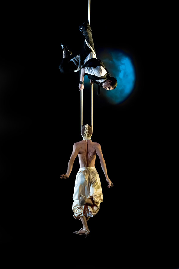 Aerial acrobat suspended in silks against a dark backdrop with blue light