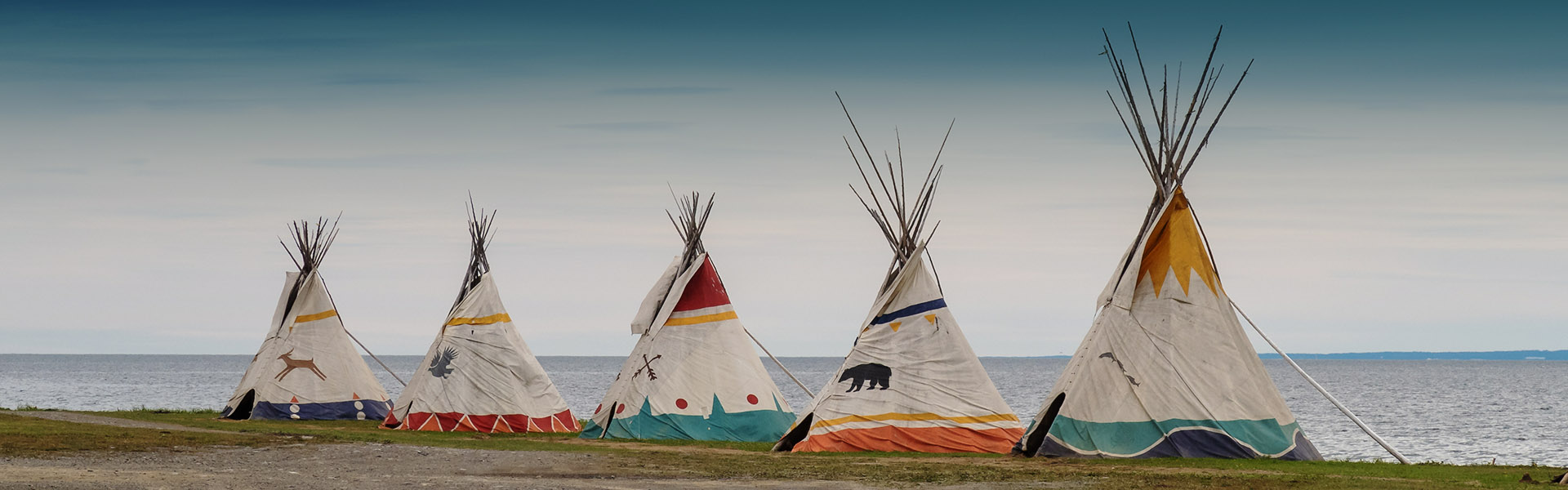 Row of decorated teepees along a shoreline